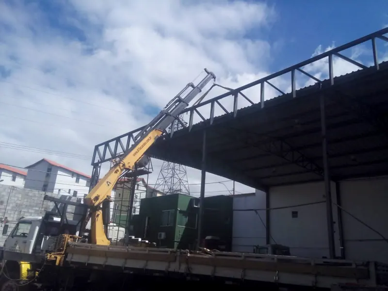 Guindaste de caminhão montando a estrutura de aço de uma cobertura