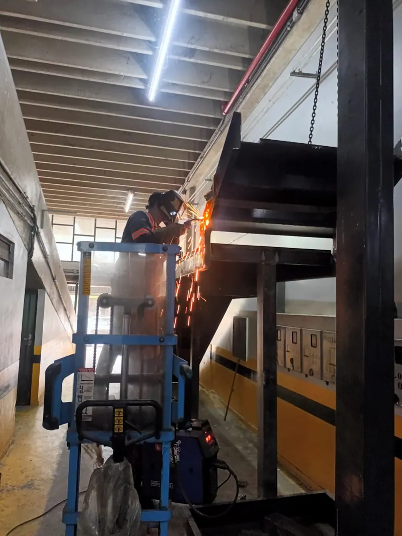 Soldador numa plataforma elevatória soldando uma estrutura alta, com faíscas